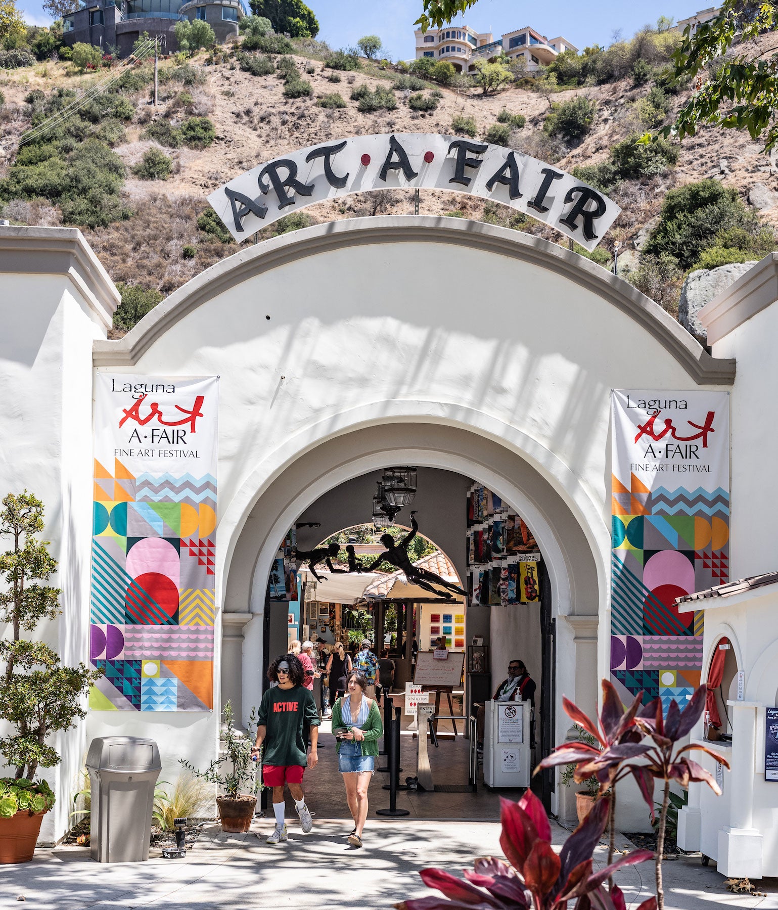 Laguna Art A-Fair summer art festival entrance with people walking through, set against a mountainous background.