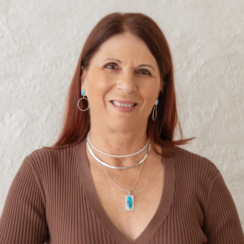 Woman wearing a brown sweater and multiple necklaces with a pendant against a light background