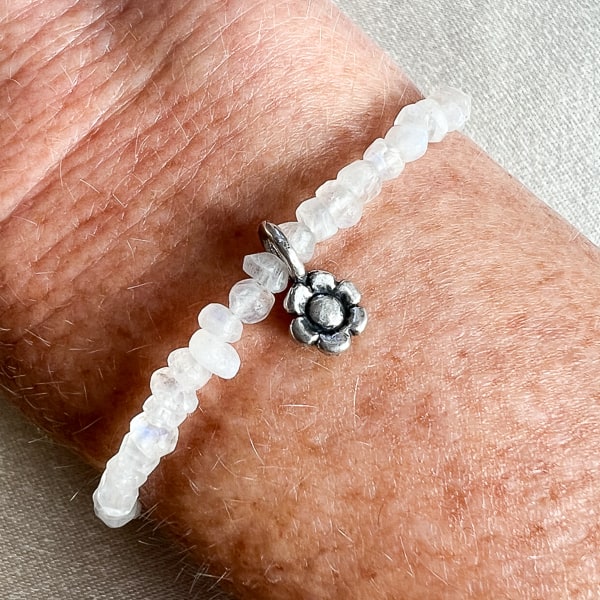 Rainbow faceted moonstone gems with a silver flower charm worn on the wrist. 