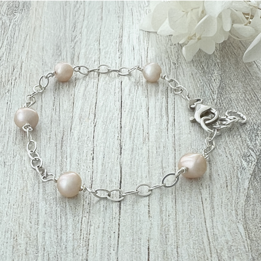 Freshwater pearl and sterling silver bracelet with creamy pearls and oval chain on wood background, showcasing soft luster and clasp detail.