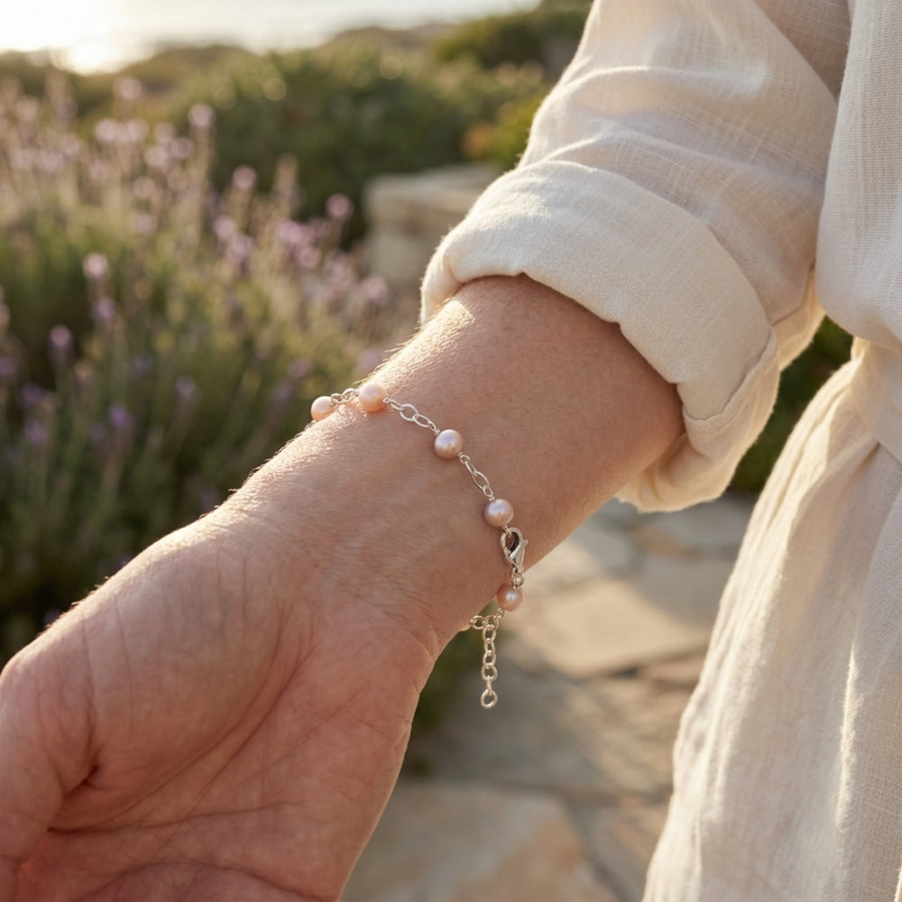 Person wearing a pearl bracelet with a blurred lavender field in the background
