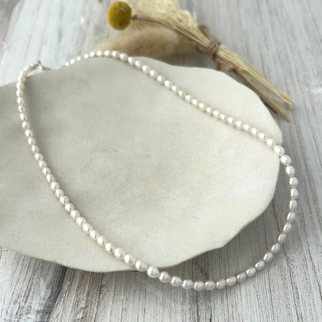 Pearl necklace on a stone surface with dried flowers in the background