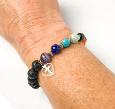 Semi-precious Gemstone 7 Chakra Bracelet, Sterling Silver Open Heart with Cross Charm, Lava Stone Bracelet, 8mm Beads, Handcrafted in CA.  This soul-inspired Chakra bracelet is handcrafted with 8mm lava & gemstone beads, Sterling Silver open heart cross charm, and antique silver-plated pewter spacers. Worn on wrist.