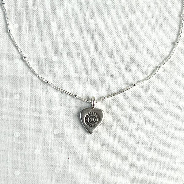 Show your love with this romantic and feminine heart necklace. Crafted from fine silver and strung along an 18” dainty chain, it is the perfect way to add a touch of delicate beauty to your everyday look. Charm detail