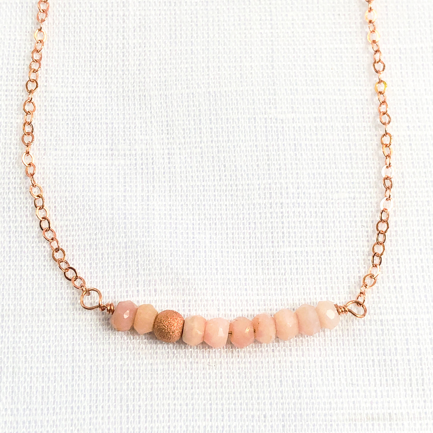 Delicate Pink Opal gemstone and Rose Gold-filled bar necklace. Perfect alone or for layering. The shine of the Rose Gold stardust bead compliments the opals nicely and gives the necklace an air of sophistication. Closeup view. Handcrafted.
