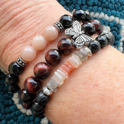 Butterfly Dreams Red Tigereye with Butterfly Charm bracelet. Deep rust red beads with whimsical butterfly charm. Worn on wrist stacked with other Novaura Jewelry gemstone bracelets.