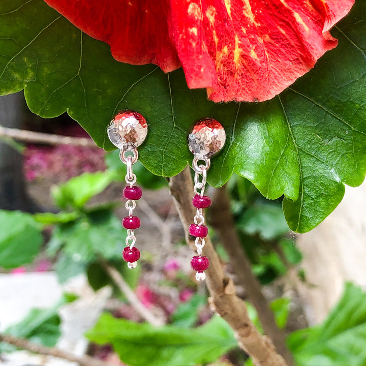 Delicate hammered finish for incredible texture to give a vintage flair to these earrings. Genuine Rubys-the queen of gems in a well-polished deep red and hand-cut rondelle shape. Lightweight in a classic round ear stud in rhodium-plated pewter. Flower styled.